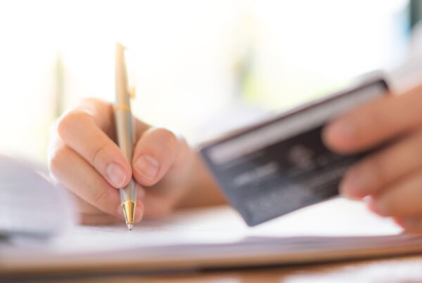 Mano che compila un documento mentre tiene una carta di pagamento, concetto di spese per i figli e gestione dell’assegno di mantenimento — Avvocato Fabrizio Tronca