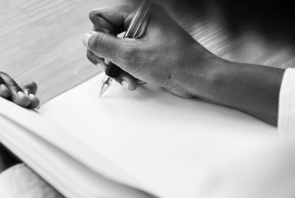 Foto in bianco e nero di una mano che tiene una penna nell'atto di scrivere su un foglio bianco e rappresenta il momento della scrittura del testamento olografo