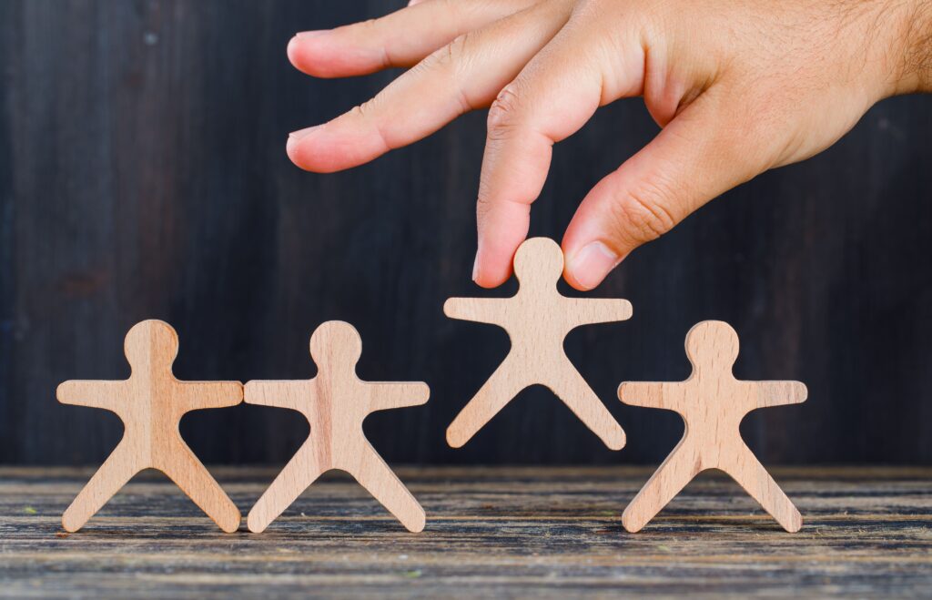 Mano che rimuove una figura umana di legno da un gruppo, simbolo dell’indegnità a succedere e dell’esclusione di un erede dalla successione.